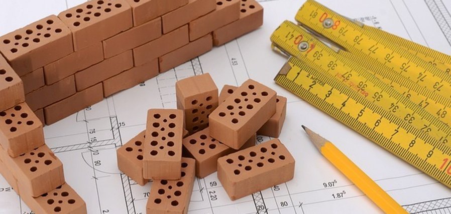 Bild von einem Bauplan mit kleinen Bausteine, Zollstock und Bleistift